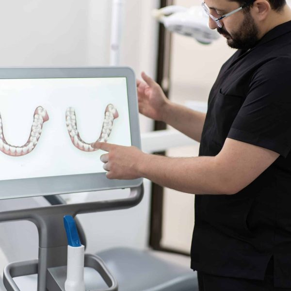 Bearded specialist in black uniform pointing to jaws models on computer screen using alternative teeth treatment methods in dental clinic oral cavity examination