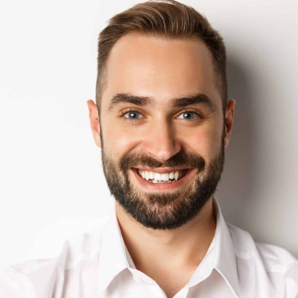 Headshot of handsome bearded man smiling, standing against white background.